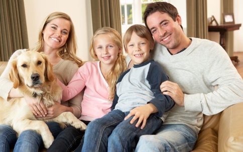 A family of four with a dog sitting on a couch in a cozy living room.