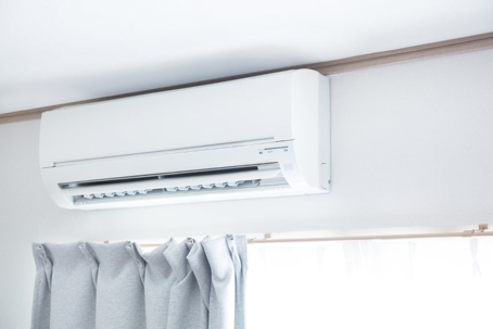 Wall-mounted air conditioner above window with gray curtains.