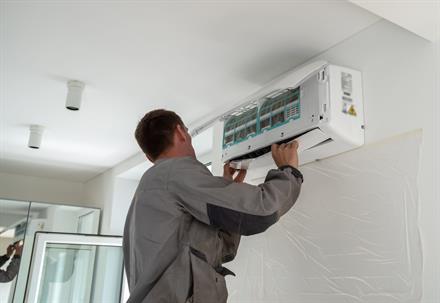 A technician installs an air conditioning unit on a wall in a room.