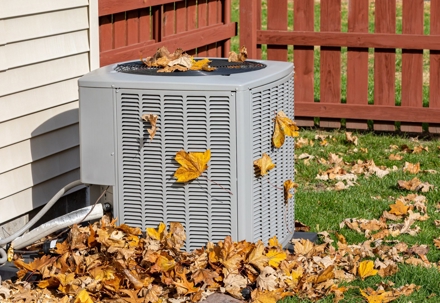 Air conditioning unit outside a house covered with fallen autumn leaves.