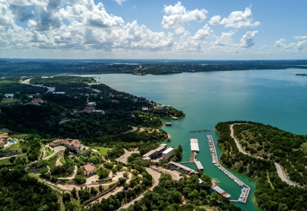 Aerial view of a scenic lake with marinas and surrounding green hills under a partly cloudy sky.