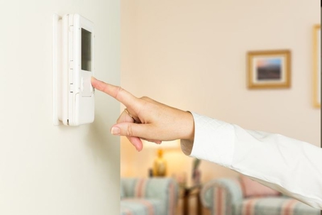 adjusting a home thermostat on a wall in a cozy living room.