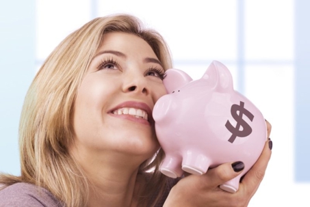 A woman smiling and holding a pink piggy bank with a dollar sign.