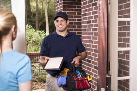 A handyman with a toolkit smiling at a woman in a doorway.