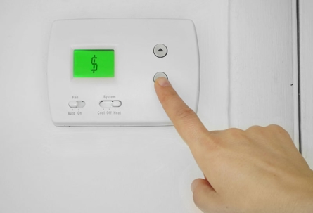 Hand adjusting thermostat with dollar sign display.