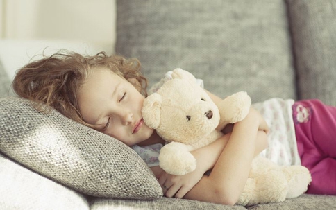 Child sleeping on a sofa cuddling a teddy bear.